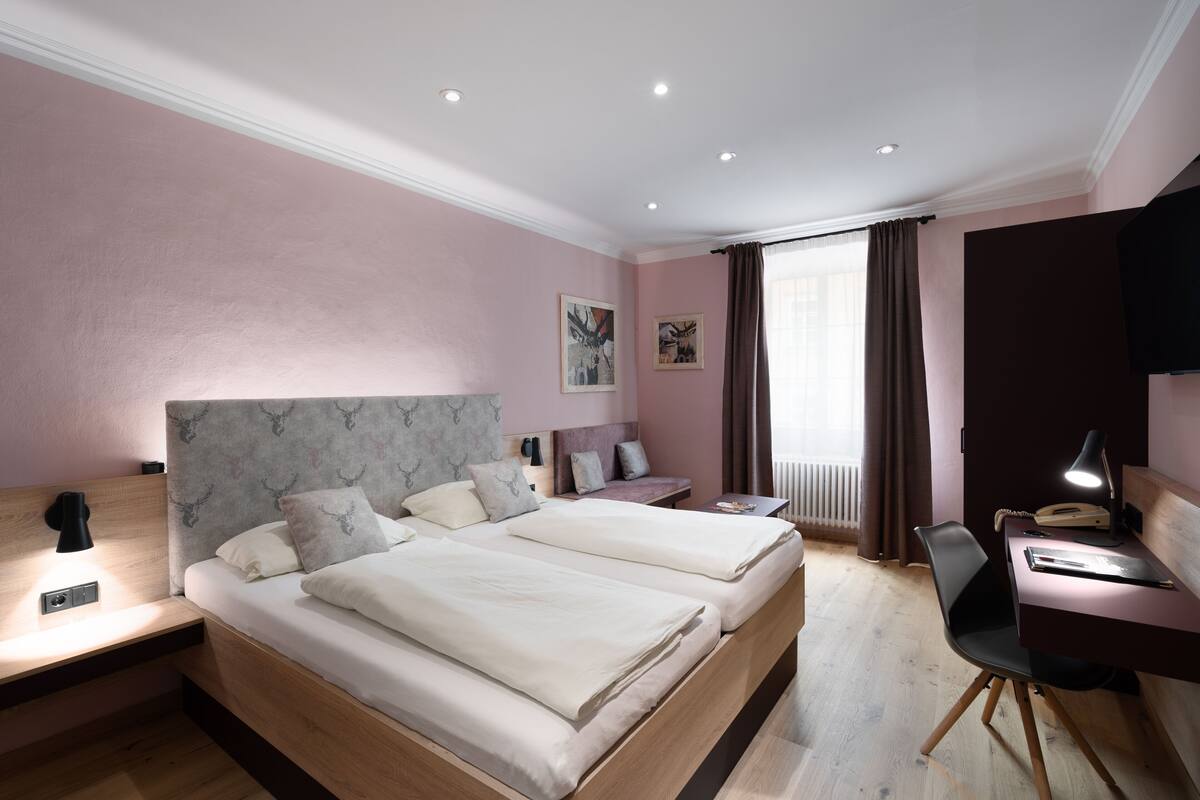 A hotel room with two beds, a desk, a chair, a desk lamp, and a TV.