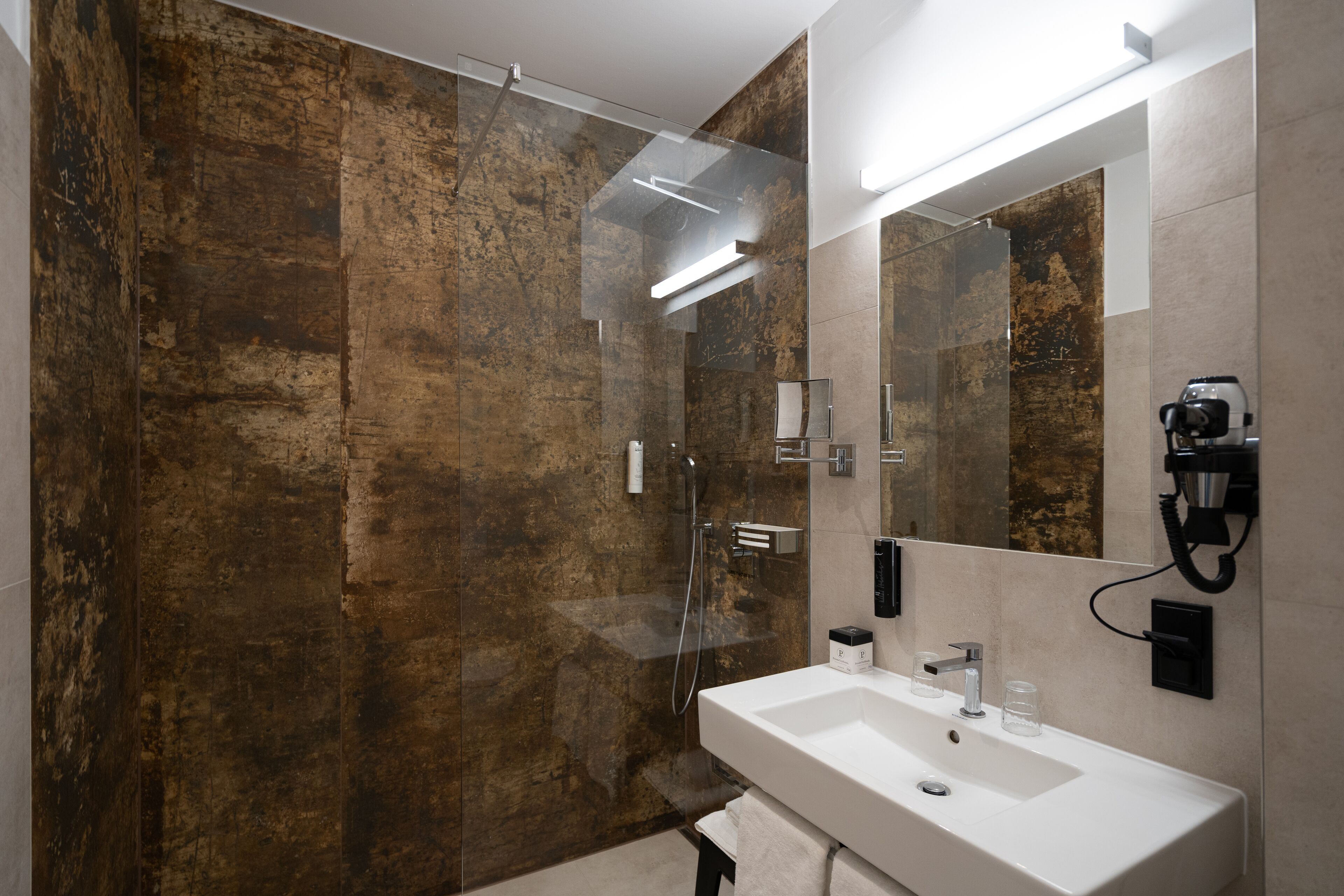 Un baño moderno con ducha de vidrio, lavamanos blanco y espejo grande.
