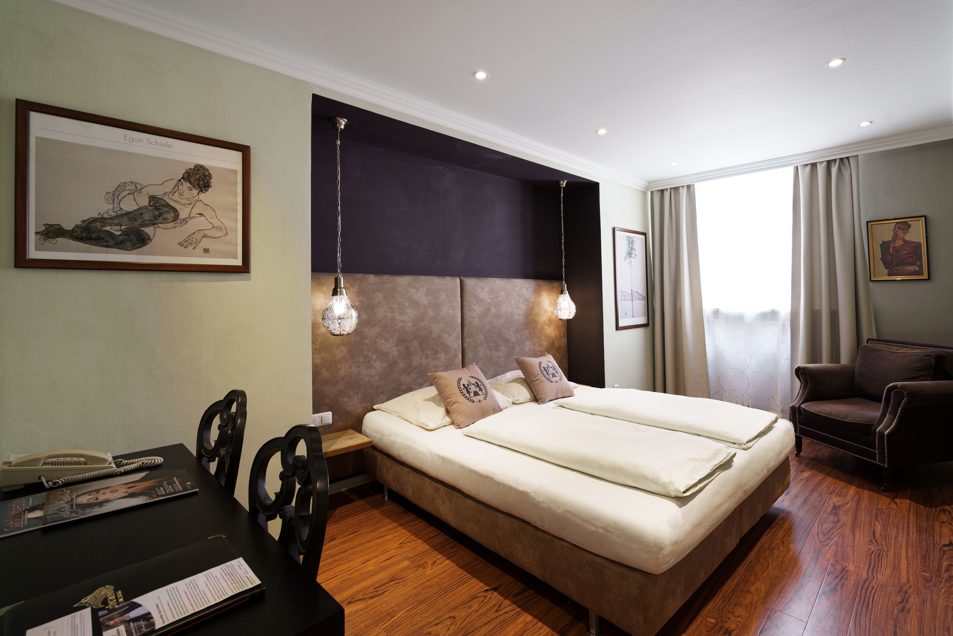 A hotel room with a large bed, a desk with a telephone, and two chairs.