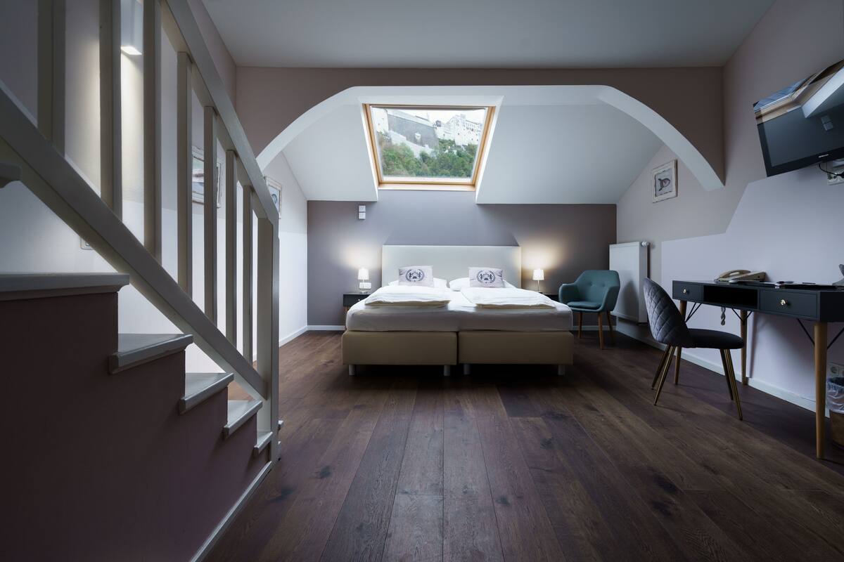 A bedroom with a skylight, a bed, bedside lamps, a desk, and a chair.
