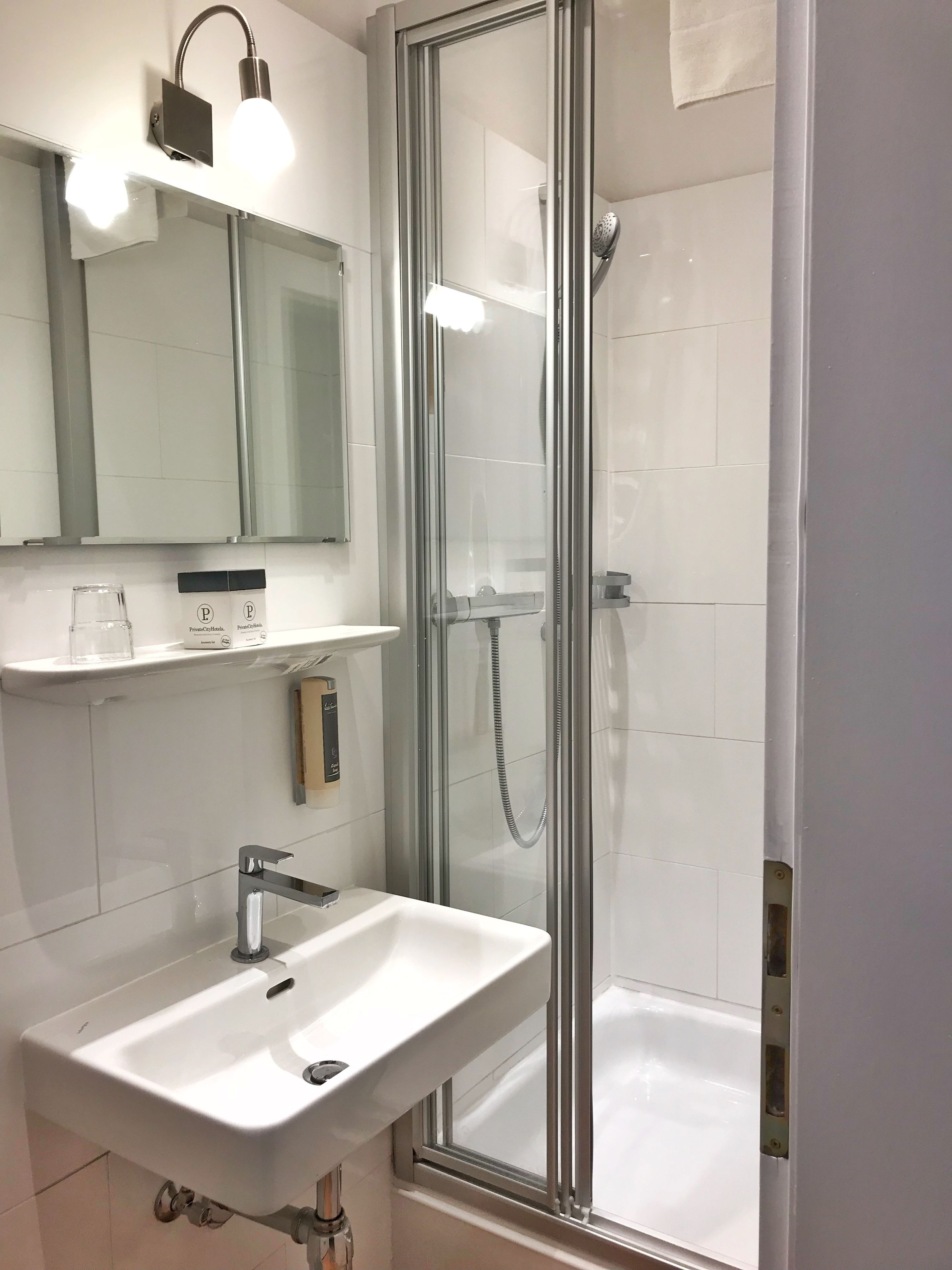 Un baño moderno con ducha de vidrio, lavamanos blanco y espejo sobre el lavamanos.