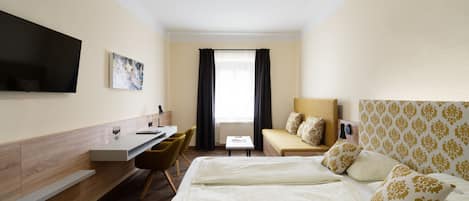 A hotel room with a bed, a desk, a chair, a television, and a window with curtains.
