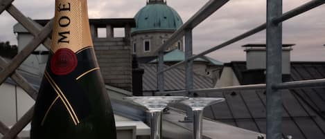 A bottle of Moët & Chandon Imperial Brut champagne and two empty wine glasses on a rooftop terrace with a view of a green-domed building.