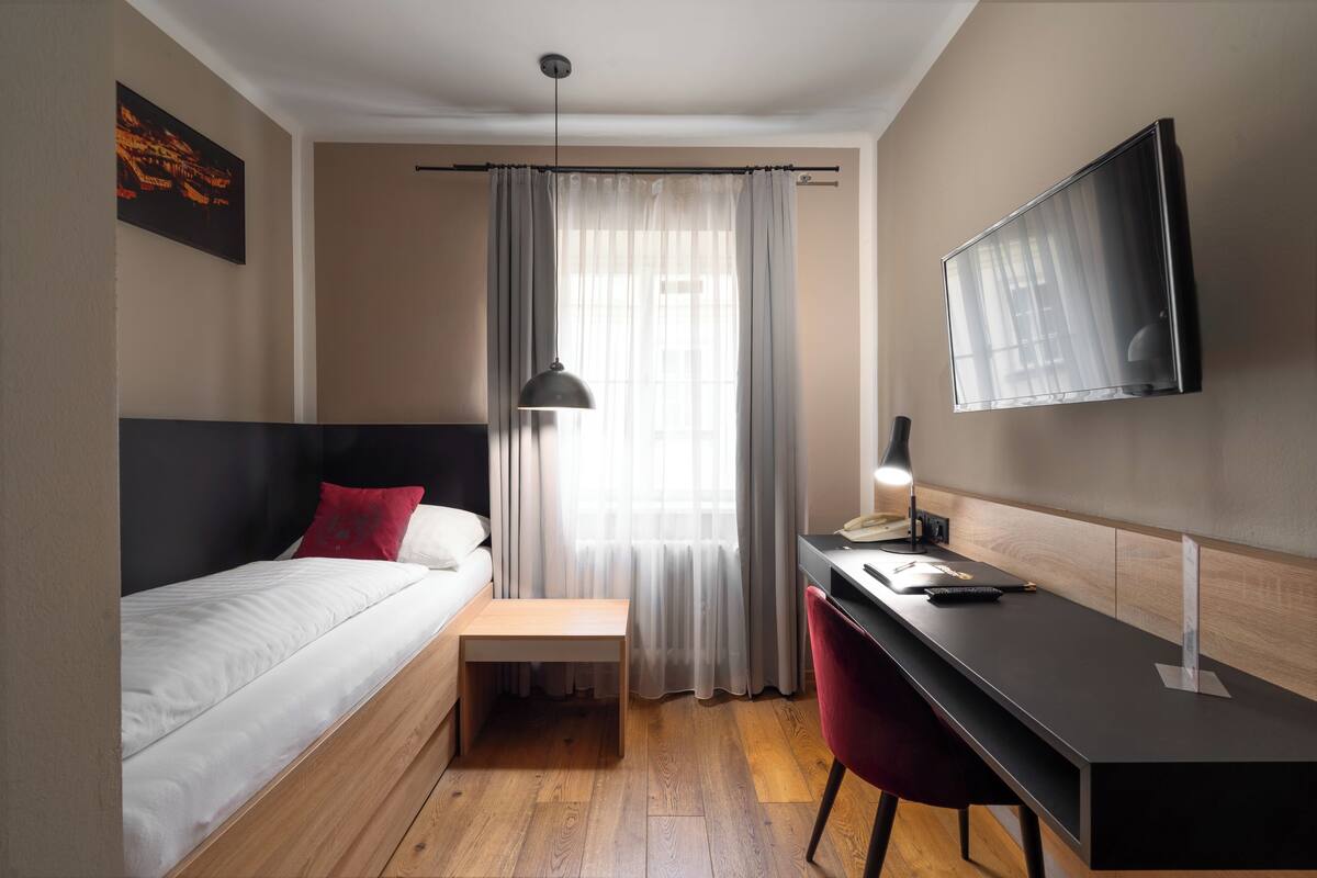 A compact hotel room with a bed, desk, chair, and a TV mounted on the wall.