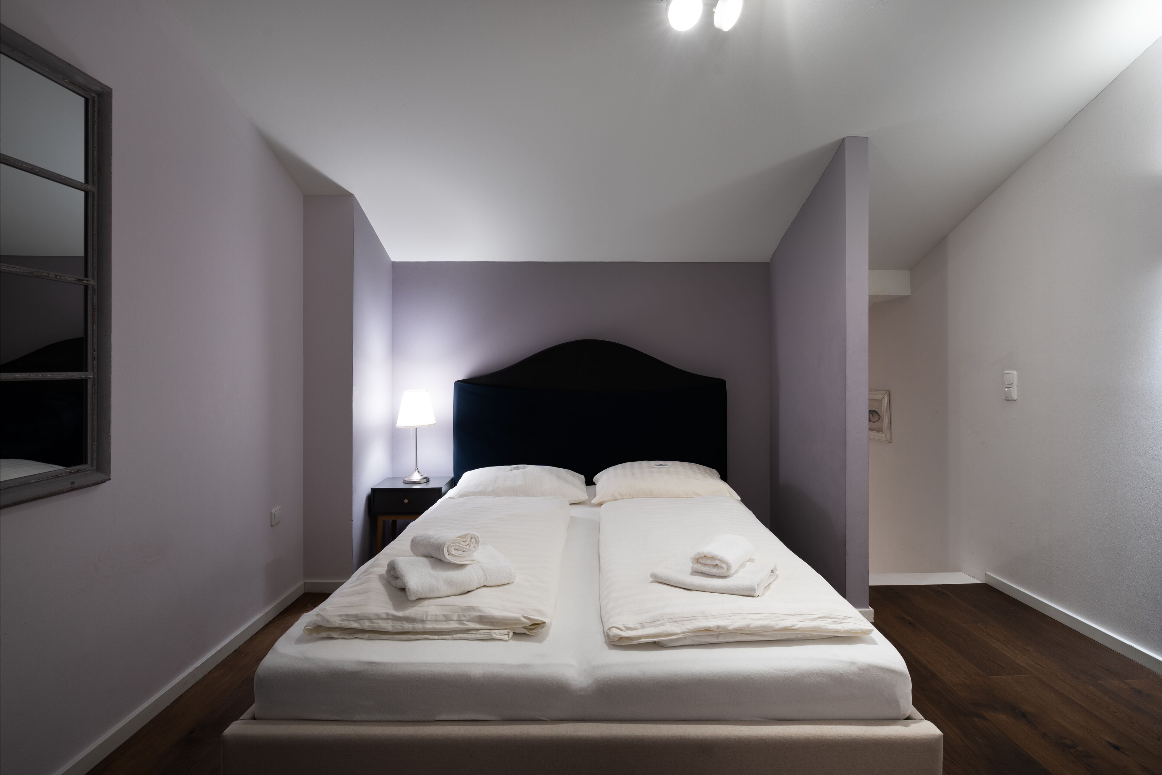 Ein Doppelbett mit weißen Leinen und Handtüchern, ein dunkles Kopfteil und ein Nachttisch mit Lampe.