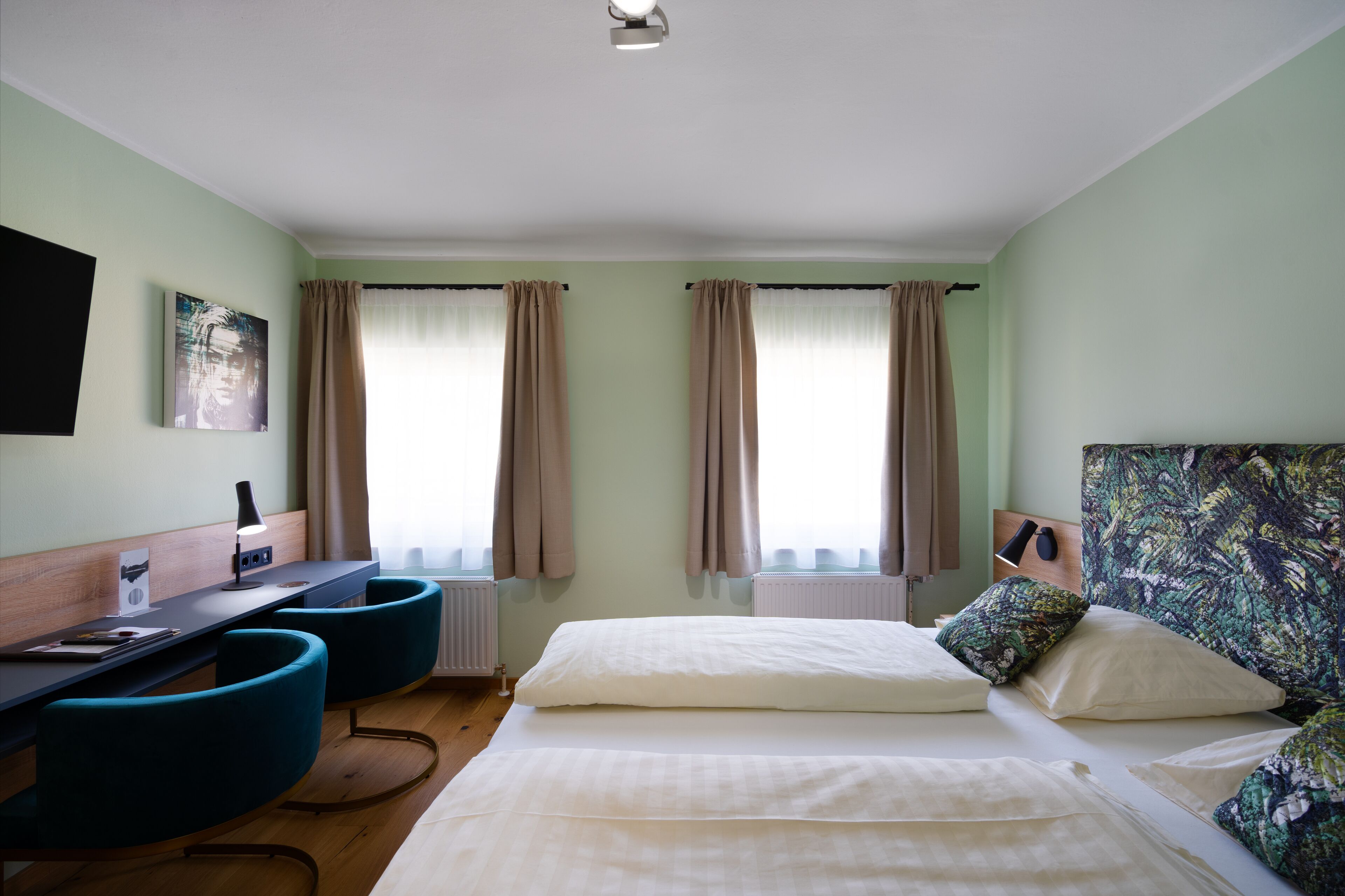 A hotel room with a bed, two chairs, a desk, a flat-screen TV, and a window with curtains.