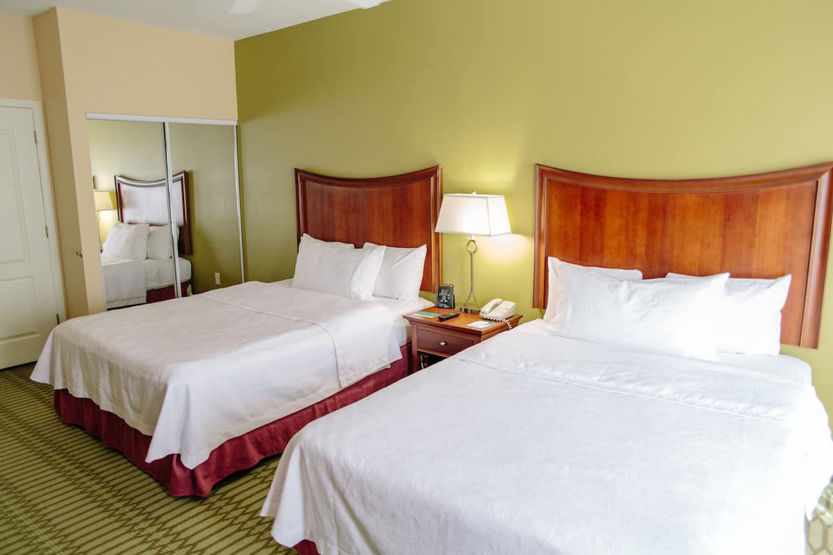A hotel room with two beds, a bedside table with a lamp, a telephone, and a mirror.