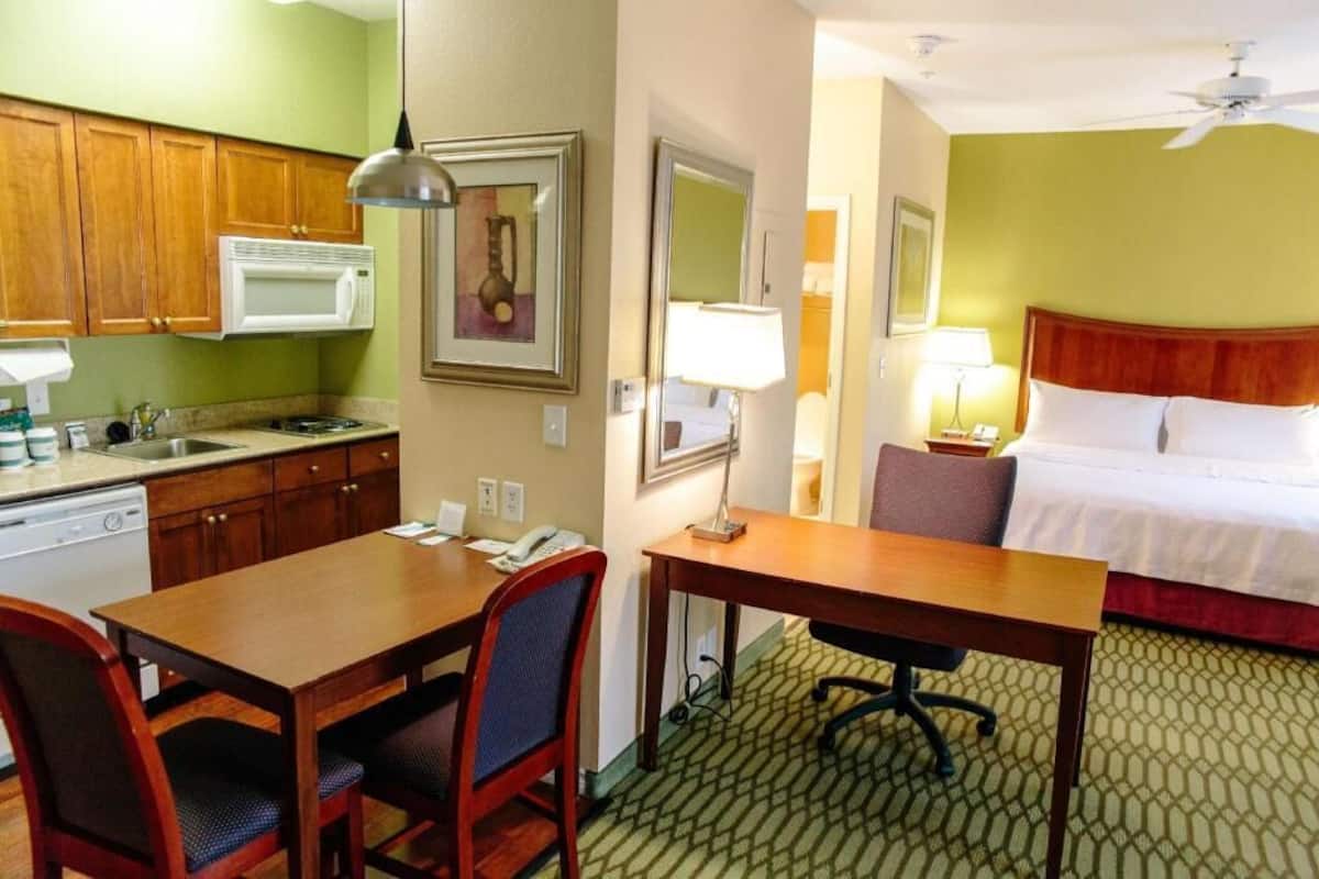 A hotel room with a bed, a desk, a chair, a microwave, a sink, and a window.