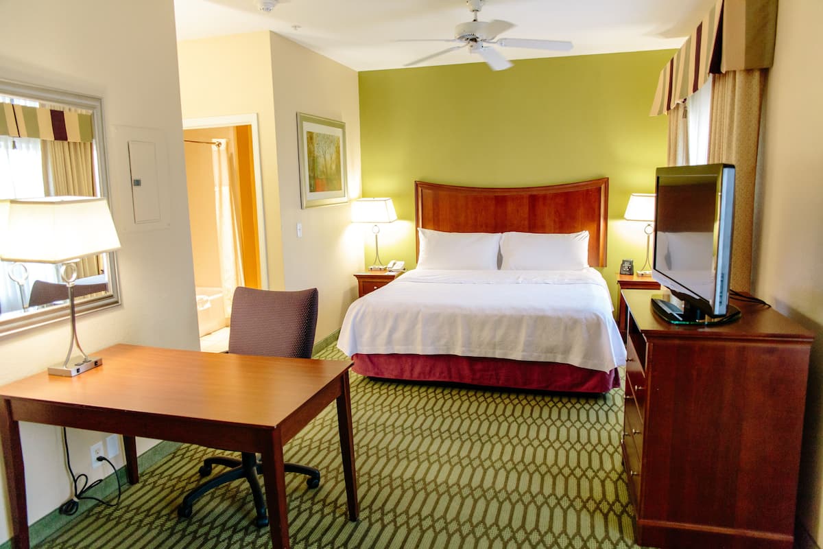 A hotel room with a bed, a desk, a chair, a television, and a ceiling fan.