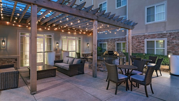 Un patio al aire libre con una pérgola, luces colgantes, mobiliario de mimbre y una chimenea de ladrillo.