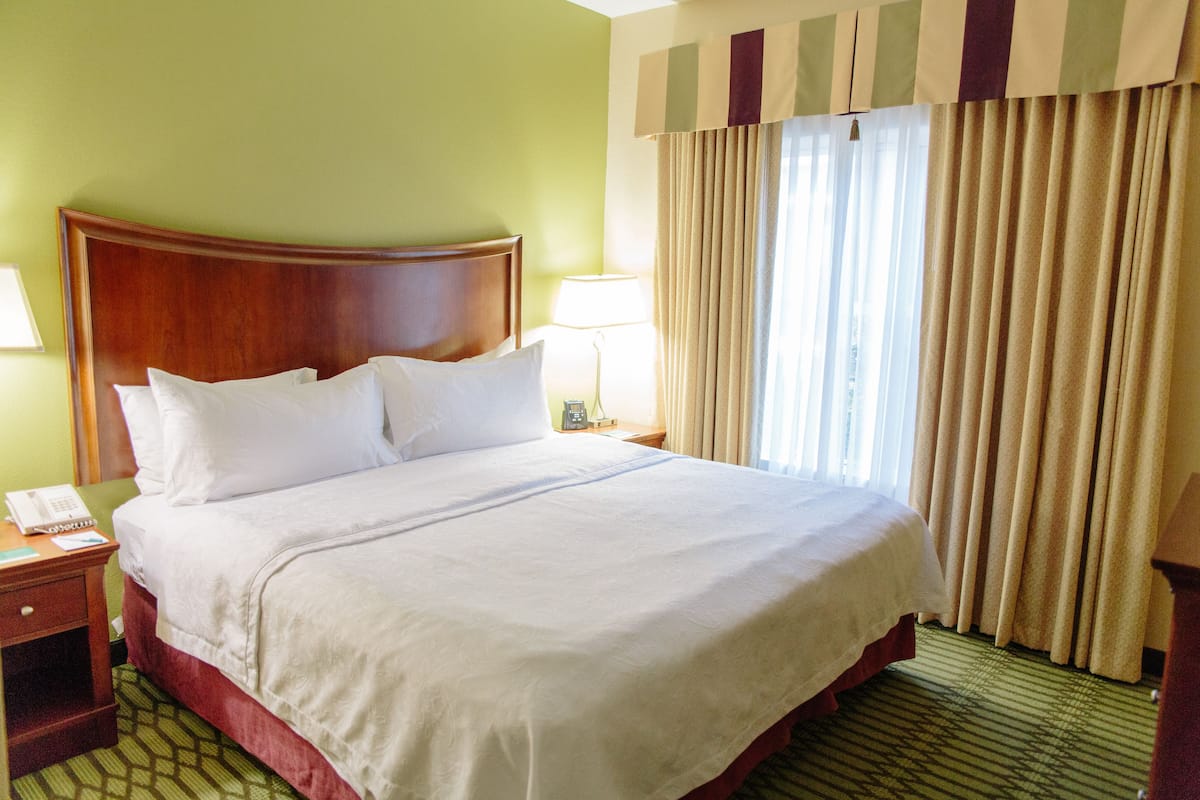 A hotel room with a large bed, a nightstand with a lamp, a telephone, and a window with curtains.