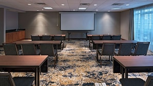 Un salón de conferencias con una pantalla grande, varias mesas y sillas.