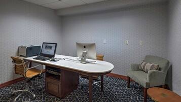 Un salón de conferencias con una gran mesa ovalada, dos computadoras de escritorio, una computadora portátil, una silla de madera y un sillón acolchado.