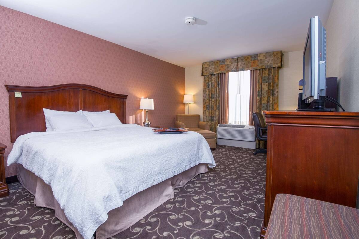 A hotel room with a large bed, two bedside lamps, a television, a desk, and a chair.