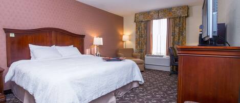A hotel room with a large bed, two bedside lamps, a television, a desk, and a chair.