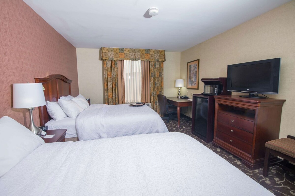 A hotel room with two beds, a desk with a lamp, a television, and a microwave.