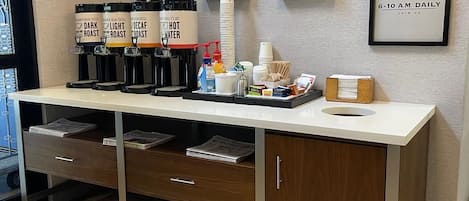A breakfast bar with coffee dispensers, a water cooler, and framed signs on the wall.