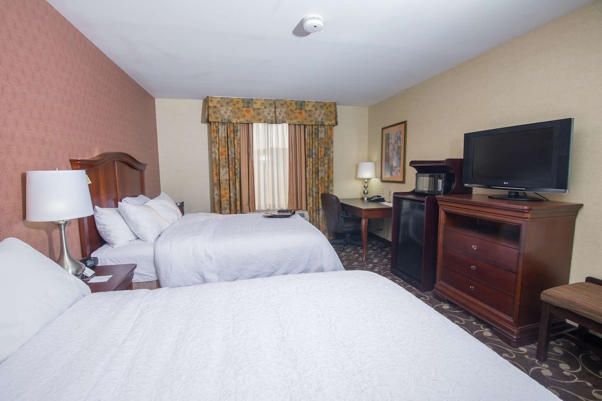 A hotel room with two beds, a desk, a television, a coffee maker, and a lamp.