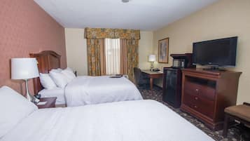 A hotel room with two beds, a desk, a television, a coffee maker, and a lamp.