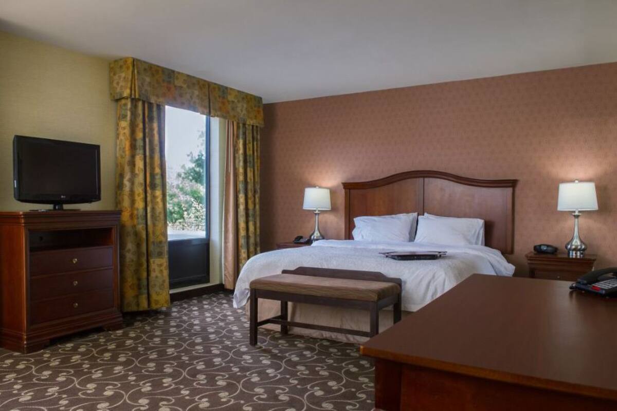 A hotel room with a bed, bedside lamps, a television, a desk, and a window with curtains.