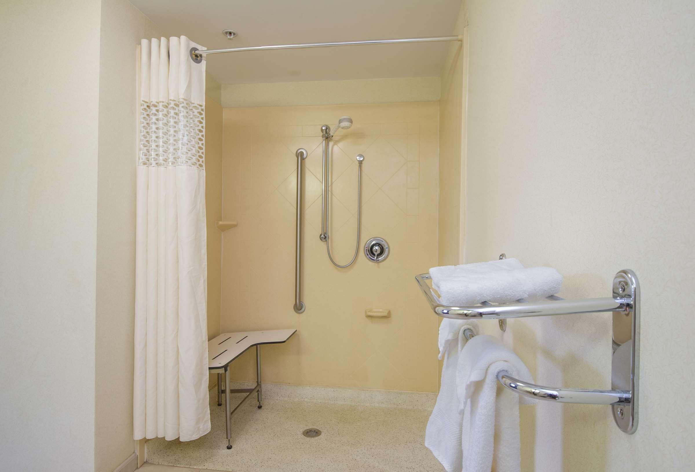 A bathroom with a shower, grab bars, a towel rack, and a small bench.