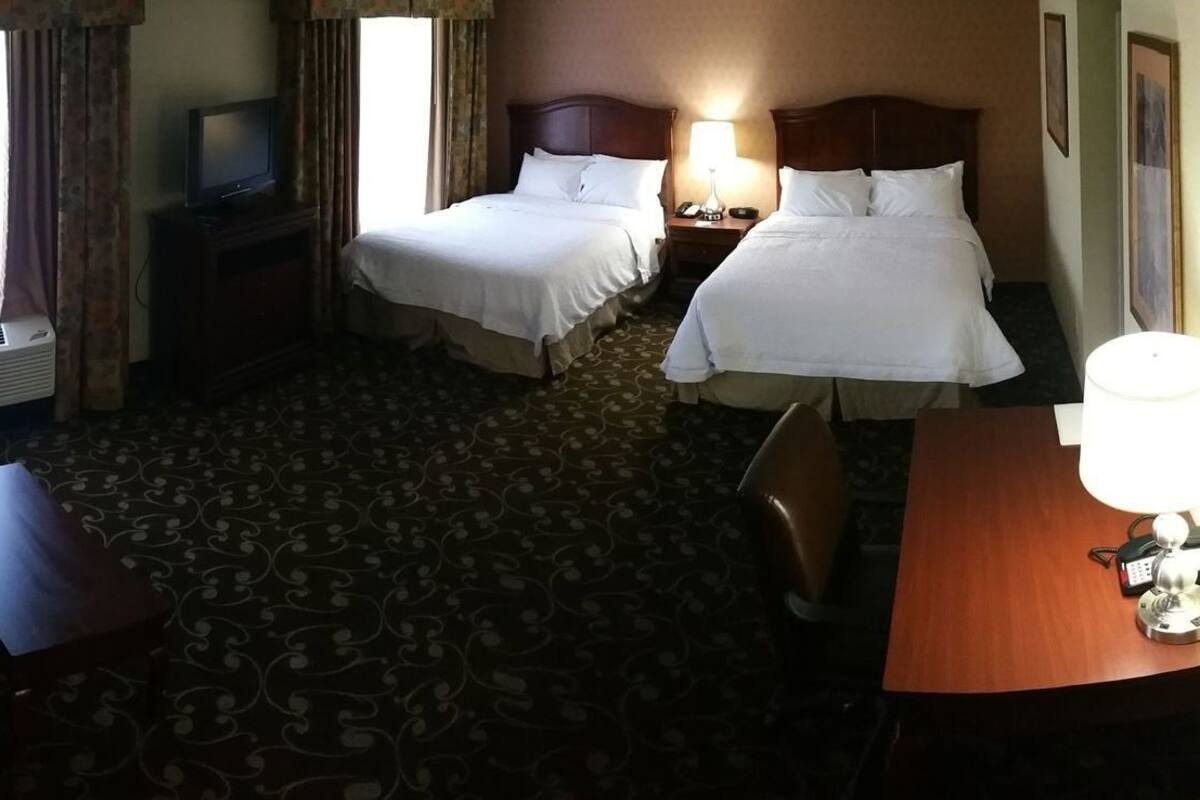 A hotel room with two beds, a desk with a lamp, a TV, and a minibar.