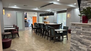A modern dining area with a large table and chairs, a kitchen in the background, and a stone accent wall. - Hampton Inn Brattleboro (Brattleboro)