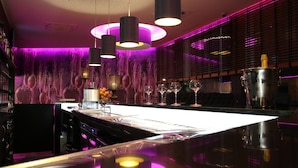A bar area with a reflective countertop, pendant lighting, and a backdrop of abstract wall art. - Hôtel de l'Univers Liège (Liege)
