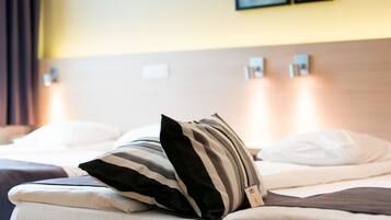 Quarto de hotel com cama bem arrumada, almofadas listradas e cabeceira com luzes fixadas na parede.