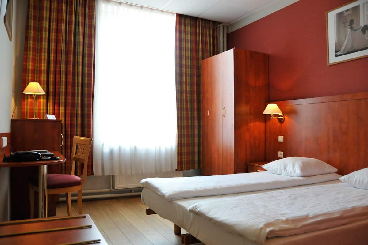 Une chambre d’hôtel avec deux lits, un bureau avec une chaise, une armoire et deux lampes.