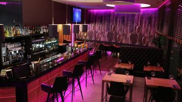 Een bar met een toonbank, barstoelen en een zithoek met tafels en stoelen.