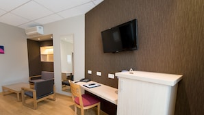 A hotel room with a wooden desk, a chair, a flat-screen TV mounted on the wall, and a small cabinet. - Hôtel de l'Univers Liège (Liege)