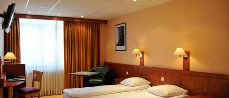 A hotel room with two beds, a desk with a chair, a television, and a window with curtains.