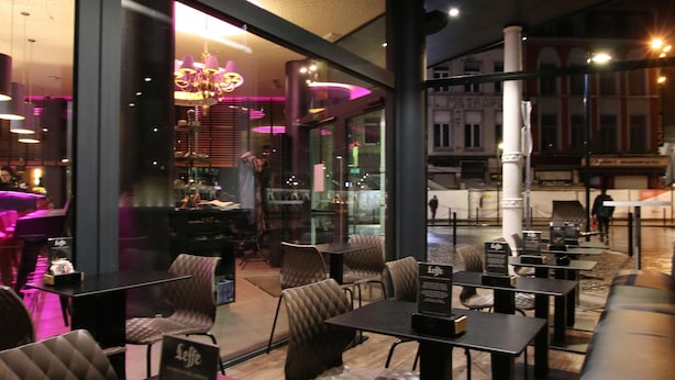 A modern indoor seating area with tables and chairs, a chandelier, and large windows. - Hôtel de l'Univers Liège (Liege)