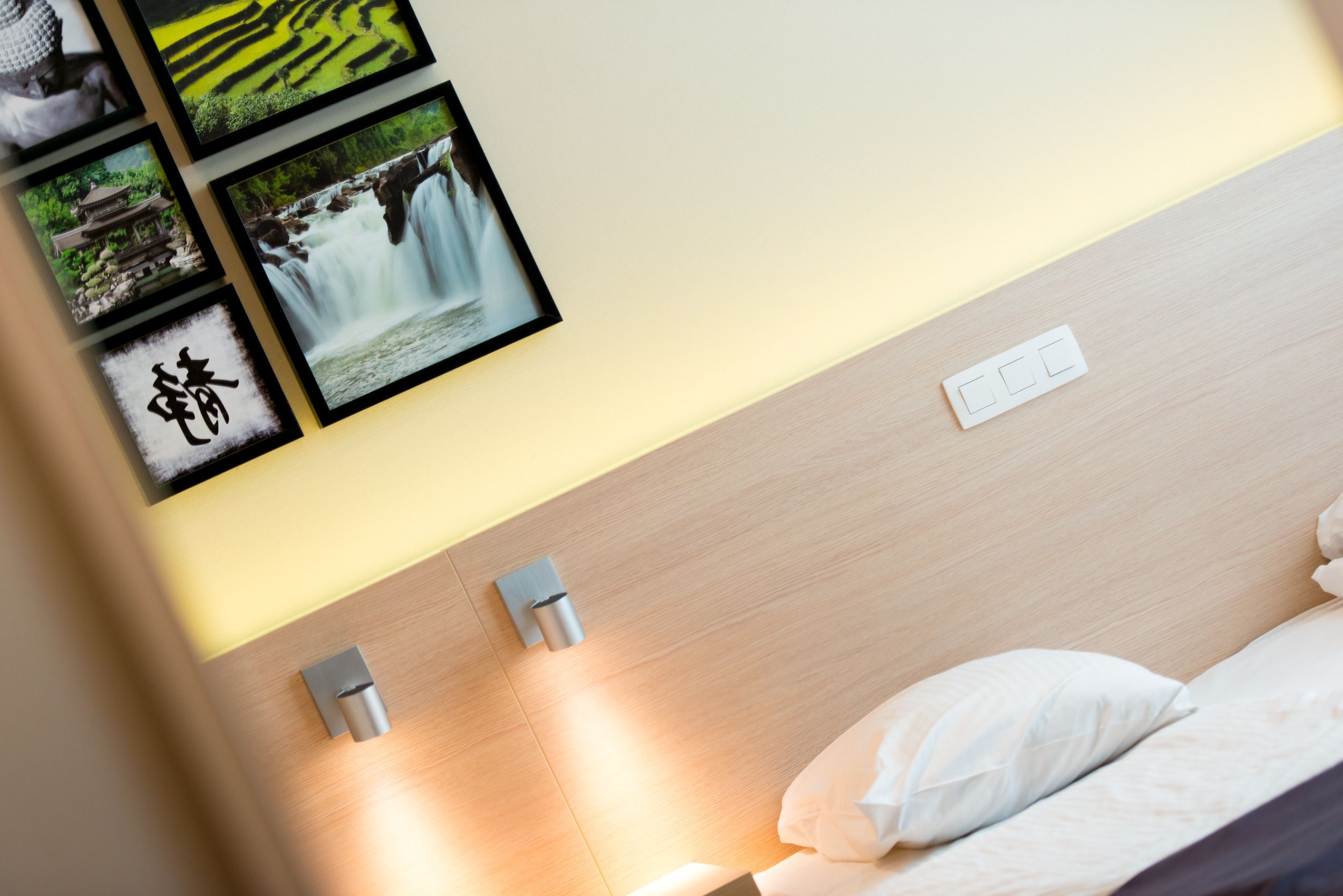 Une chambre d’hôtel avec une tête de lit en bois, un lit avec une literie blanche et un interrupteur fixé au mur.
