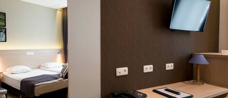 A hotel room with a bed, bedside table, lamp, and a mounted TV.