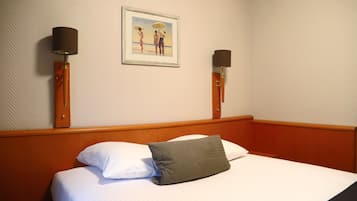 A hotel room with a bed, a framed picture on the wall, and two wall-mounted lamps.