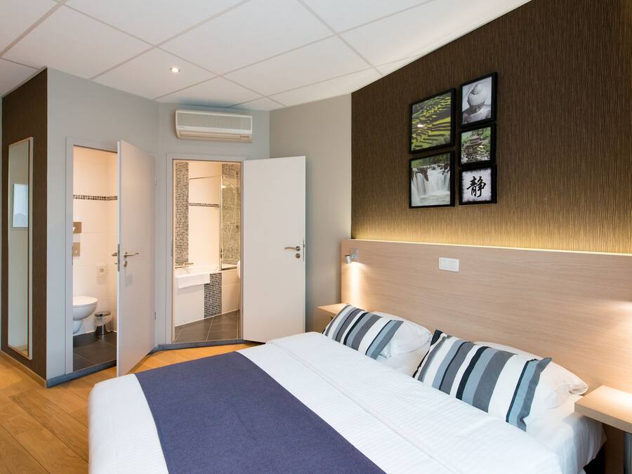 A hotel room with a large bed, a bedside table, a wall-mounted TV, and a bathroom visible through an open door.