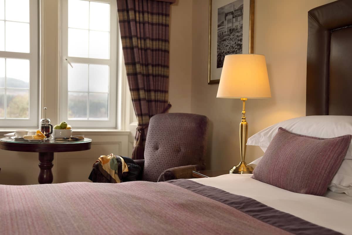 Ein Hotelzimmer mit einem Bett, einem Sessel, einem Tisch mit Lampe und einem Fenster mit Vorhängen.
