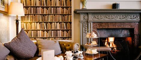 Una biblioteca con estanterías, una chimenea y una mesa con té y pasteles.