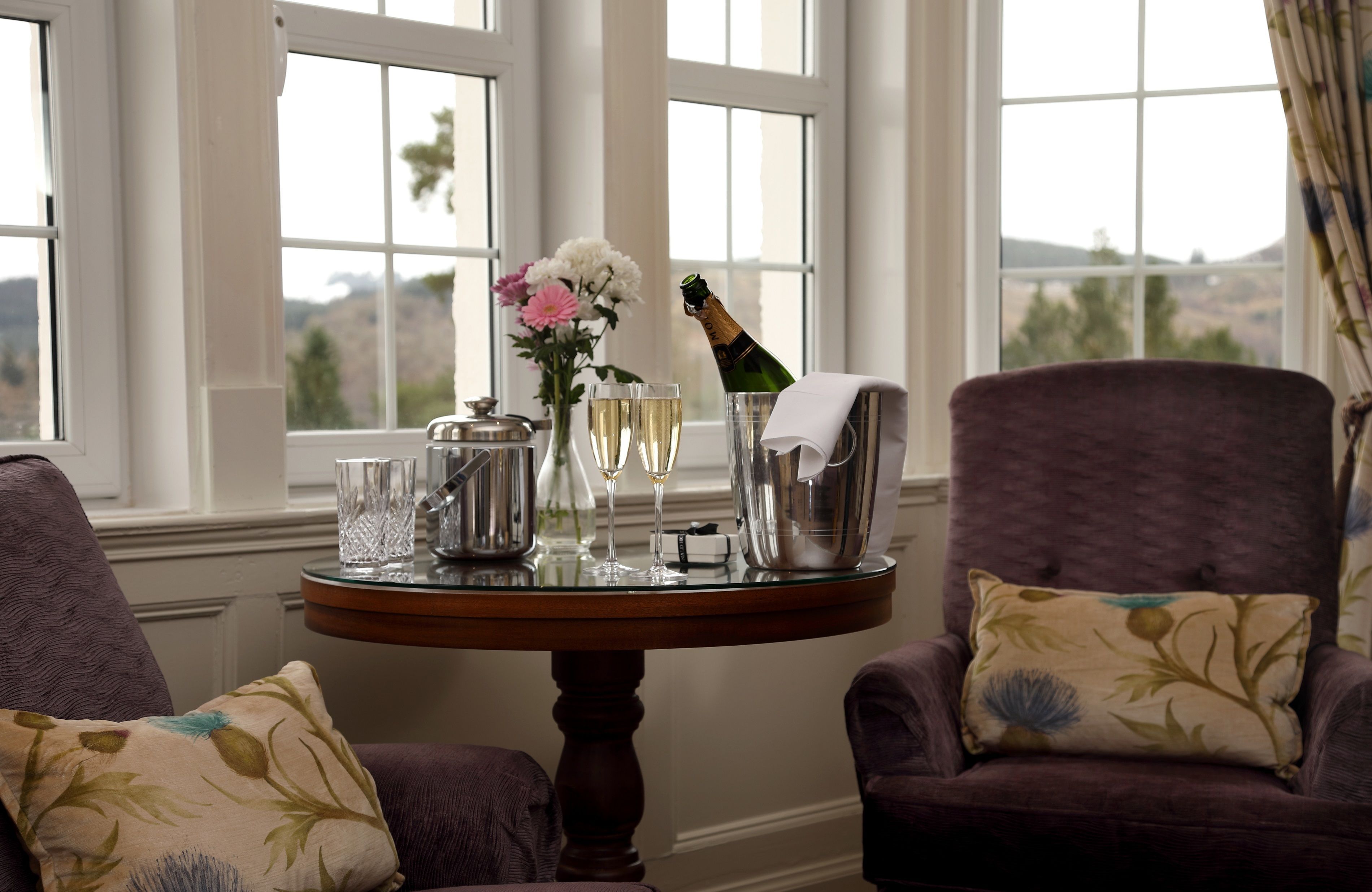 A room with a table set for a celebration, featuring a bottle of champagne, glasses, a vase with flowers, and a decorative pitcher.