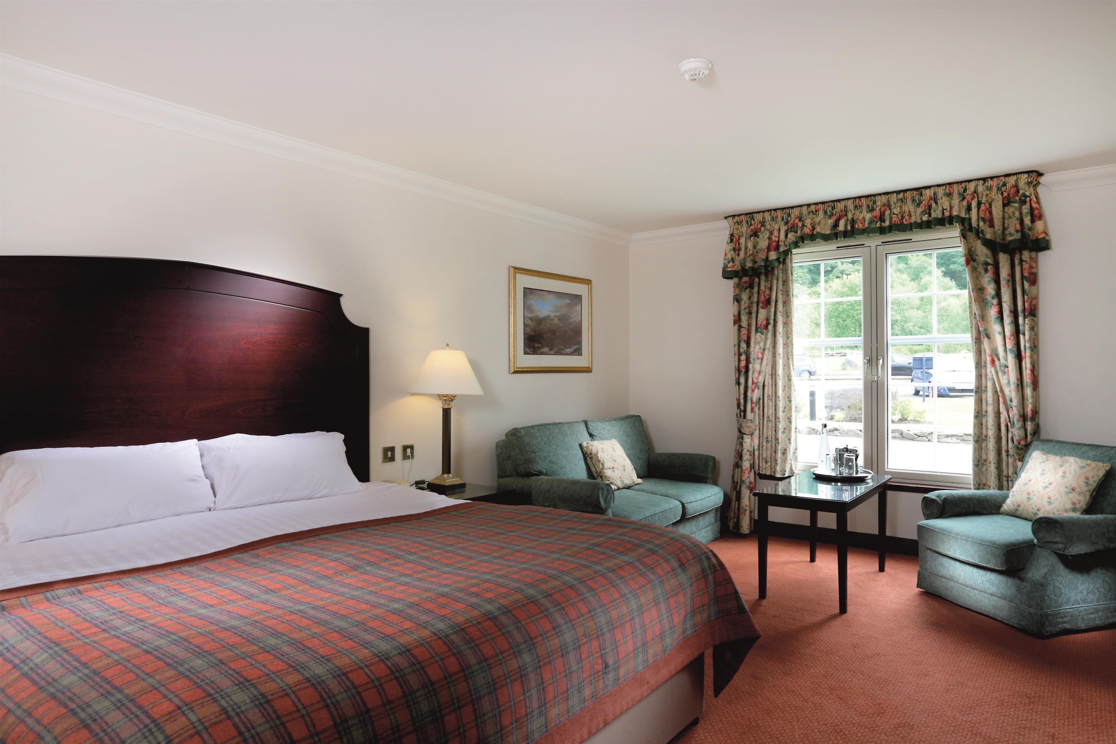 A hotel room with a large bed, two armchairs, a small table, and a window with curtains.