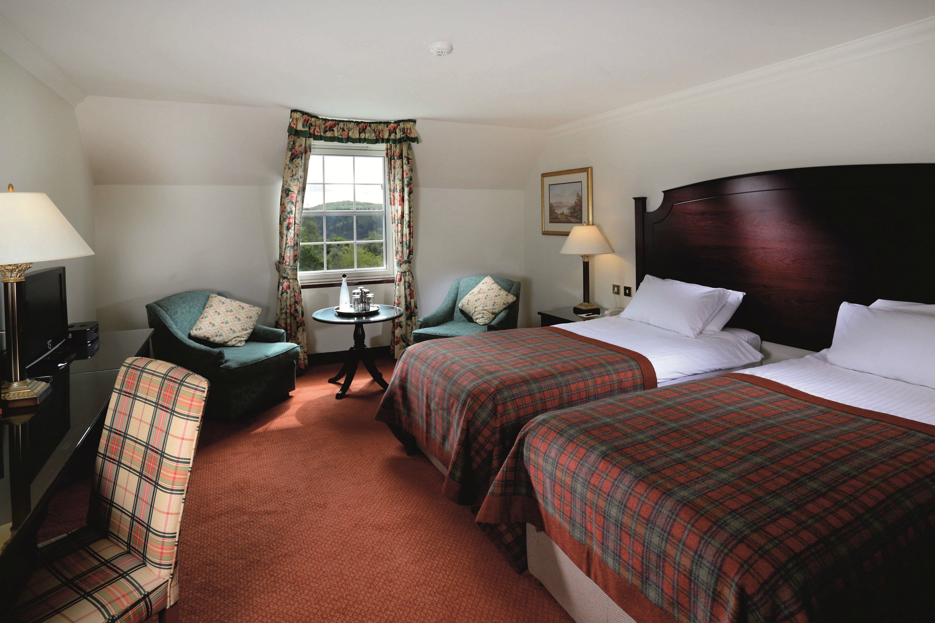 A hotel room with two beds, a desk, a chair, a television, and a window with curtains.