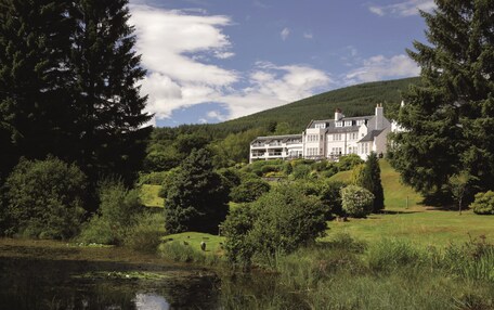 A large, white, multi-story building with a symmetrical facade, surrounded by lush greenery and a hill in the background.