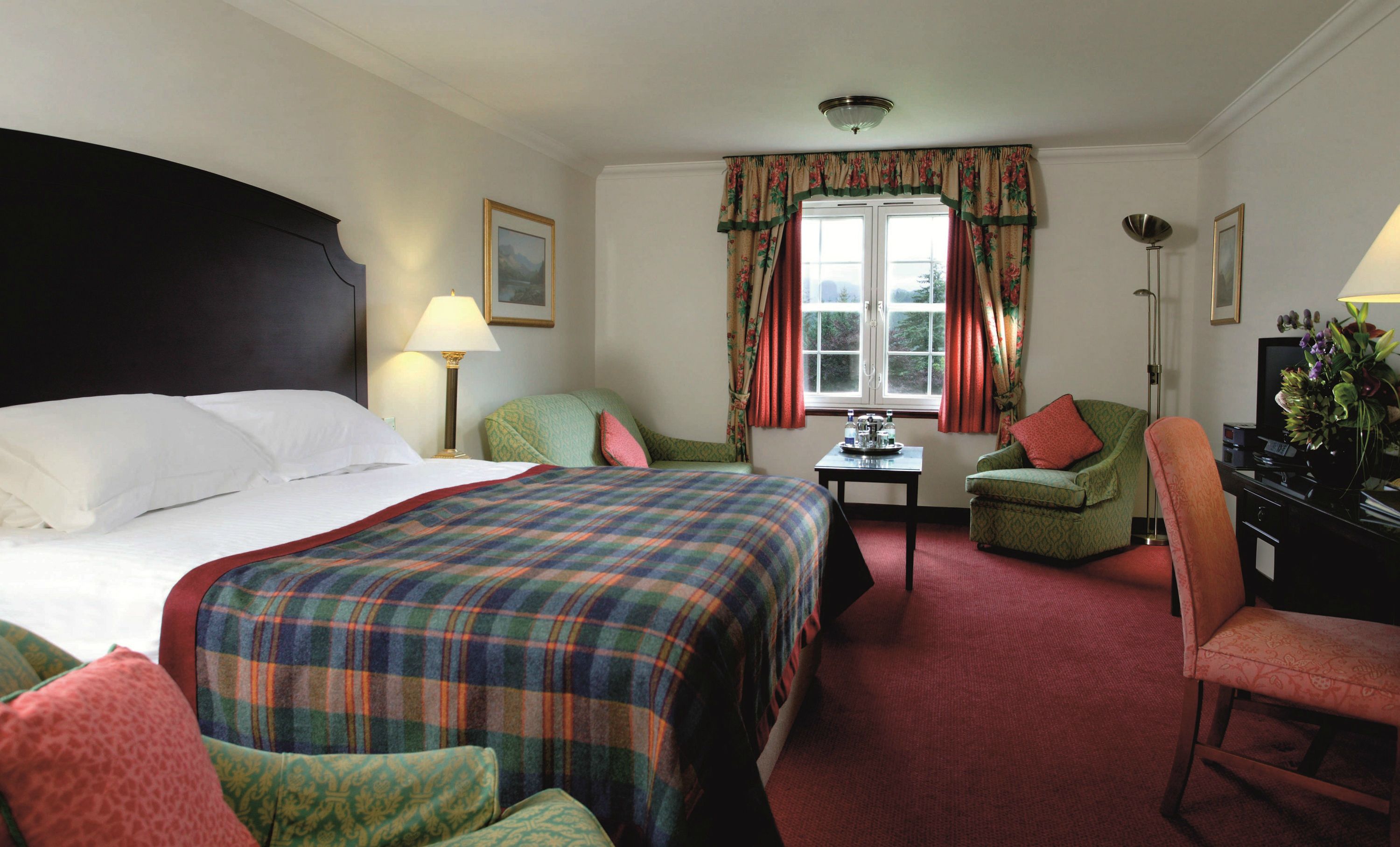 A hotel room with a large bed, two chairs, a desk, a television, and a window with curtains.