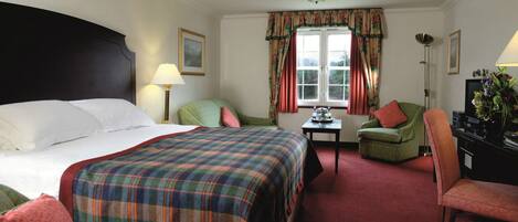 A hotel room with a large bed, two chairs, a desk, a television, and a window with curtains.