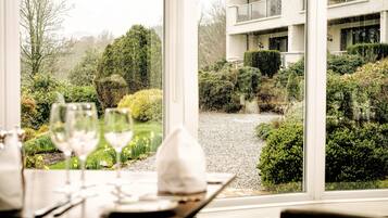Mesa de comedor con copas de vino y servilleta, con vista a un jardín cuidado y un edificio moderno con varios balcones.