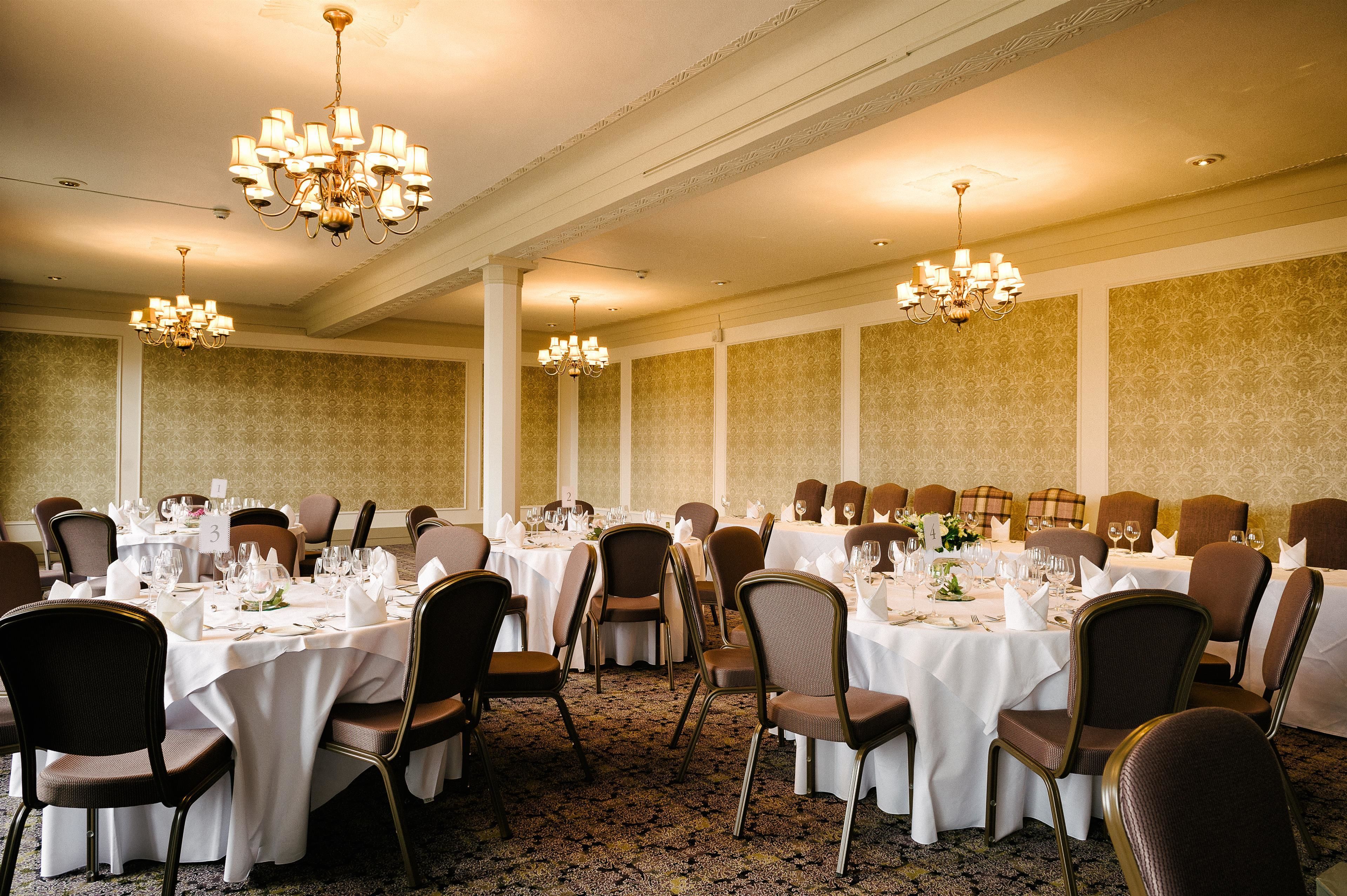 Un salón de banquetes con varias mesas redondas, cada una cubierta con manteles blancos, sillas y cubiertos.