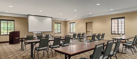 A conference room with a large table, multiple chairs, a projector screen, and windows.