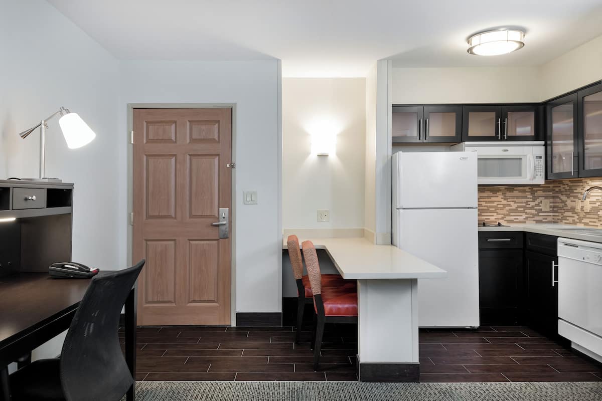 A compact kitchen with a dining area, a microwave, a refrigerator, and a wooden door.